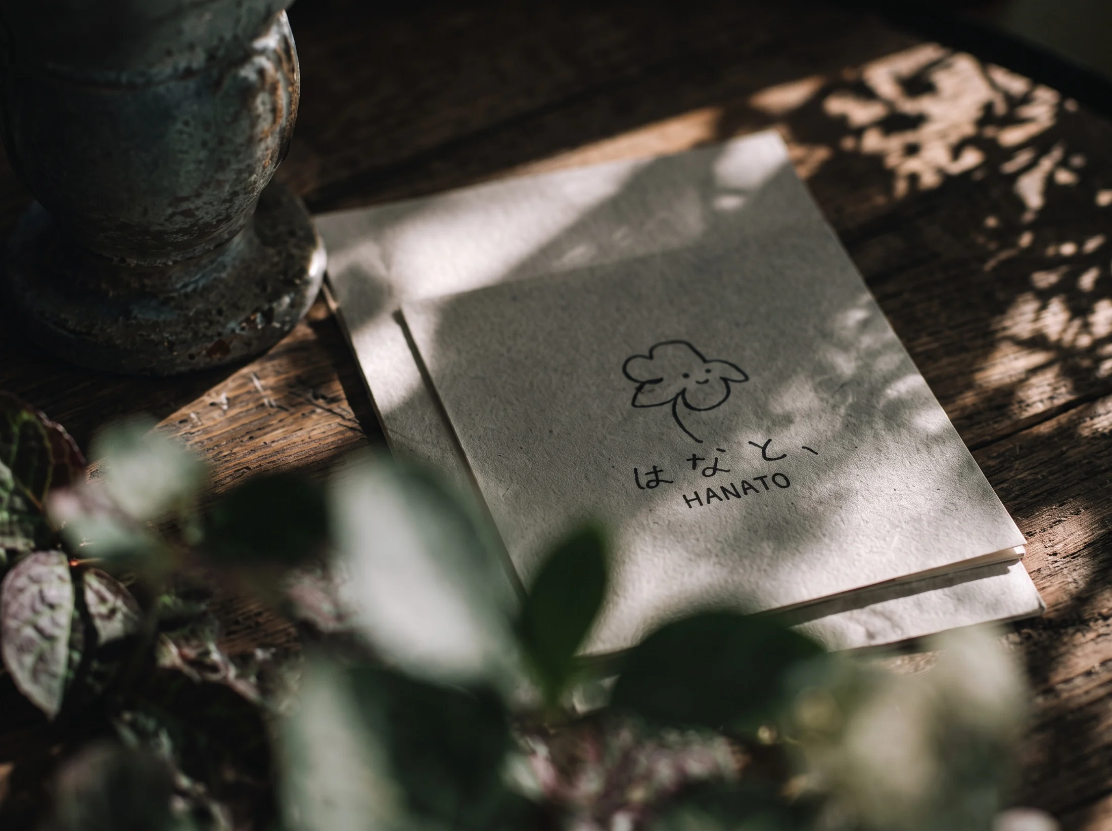 HANATO's flower mark on paper, touched by soft sunlight and leafy shadows